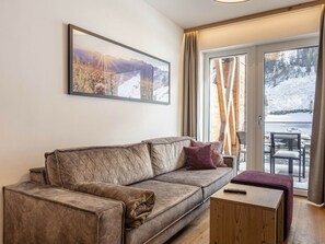 A living room with a sofa, a coffee table, and a large window with a view of a snowy landscape. - Holiday Apartment With 1 Bedroom (Rauris)