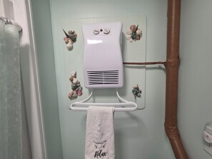 A bathroom with a towel rack holding a towel with 'Relax' text, a white heater mounted on the wall, and decorative seashells.
