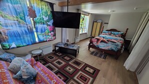Quarto com cama, escrivaninha, cadeira, televisão e janela com cortinas.
