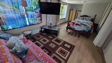 Quarto com cama, escrivaninha, cadeira, televisão e janela com cortinas.