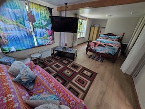 Un dormitorio con cama, escritorio, silla, televisor y ventana con cortinas.