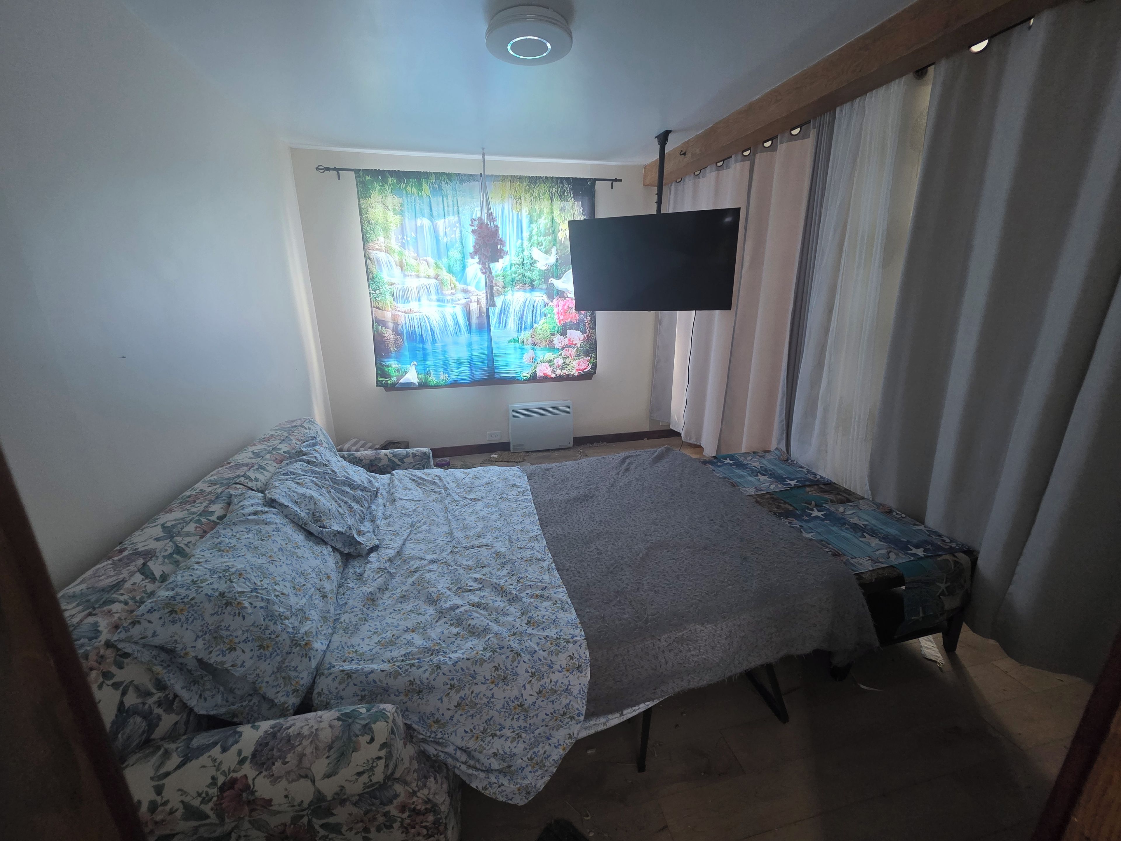 Quarto com cama, janela com cortinas, televisão de tela plana e radiador.