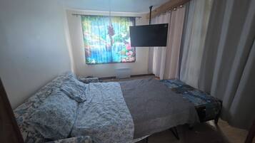 Ein Schlafzimmer mit Bett, einem Fenster mit Vorhängen, einem Flachbildfernseher und einer Heizung.