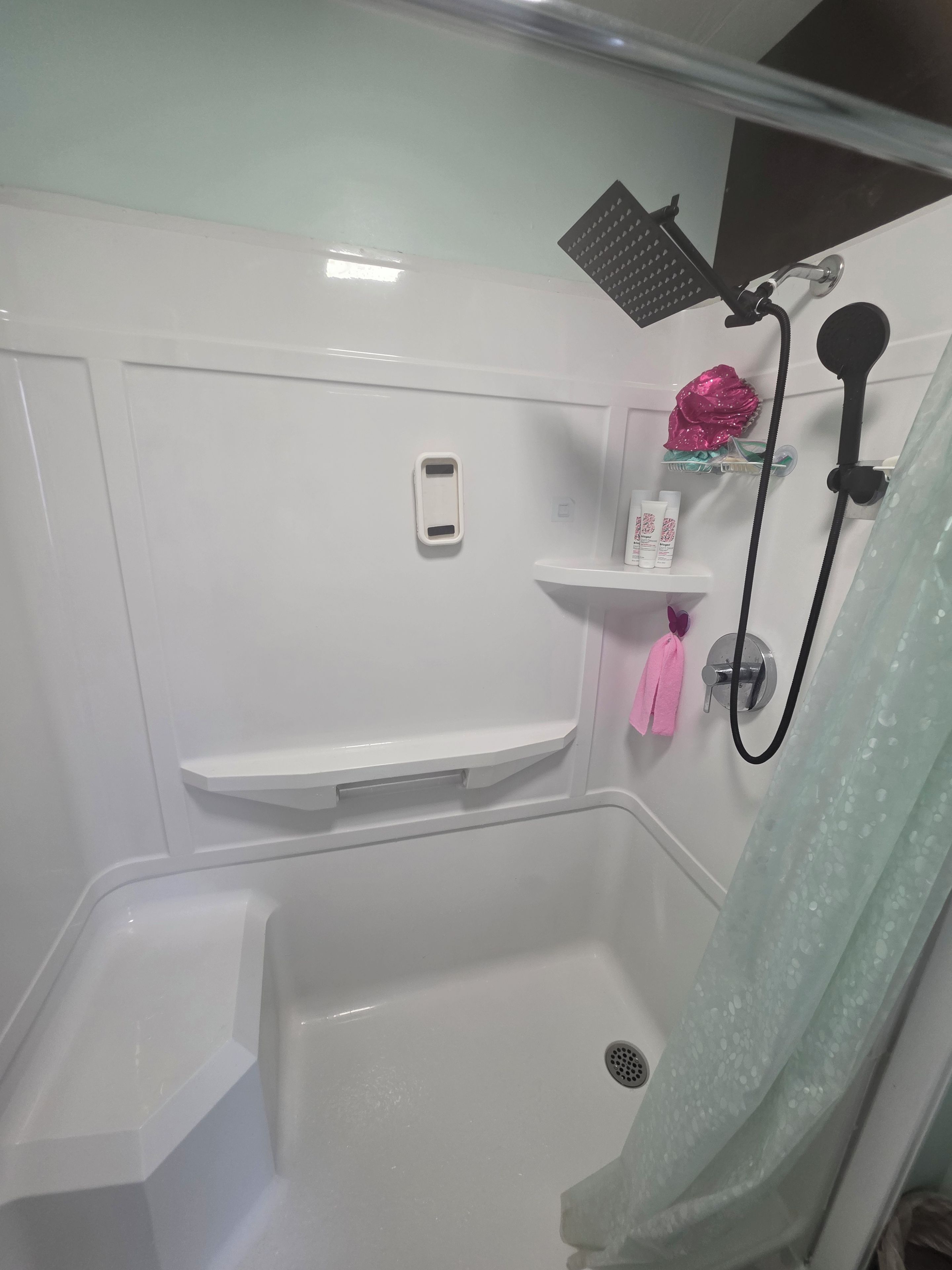 A bathroom with a shower, a vanity with a mirror, and a shelf with toiletries.