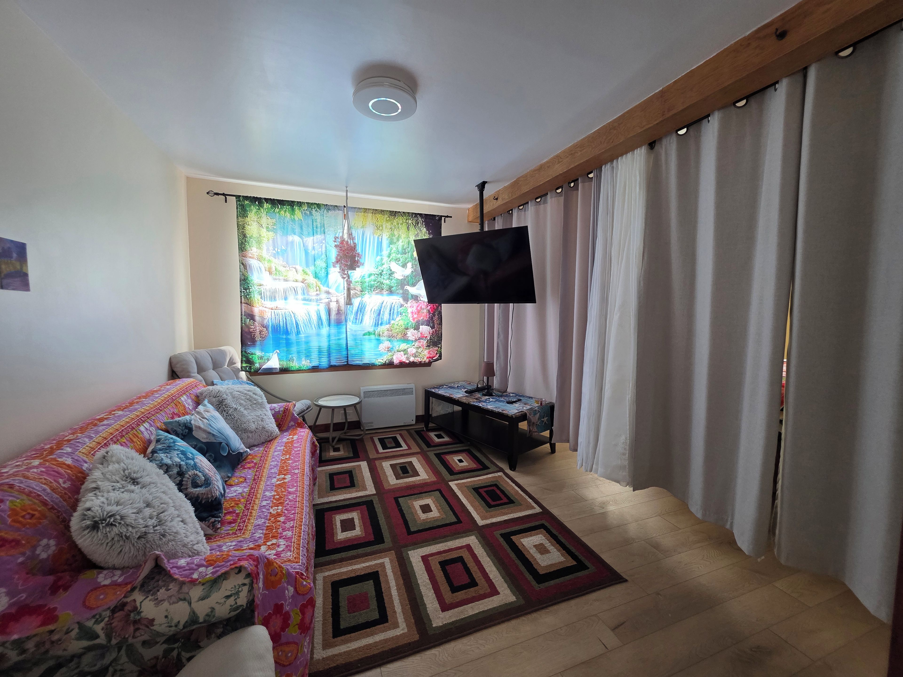 Uma sala de estar aconchegante com sofá, TV de tela plana, tapete estampado e janela com cortinas.