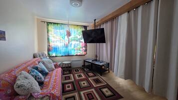 Uma sala de estar aconchegante com sofá, TV de tela plana, tapete estampado e janela com cortinas.