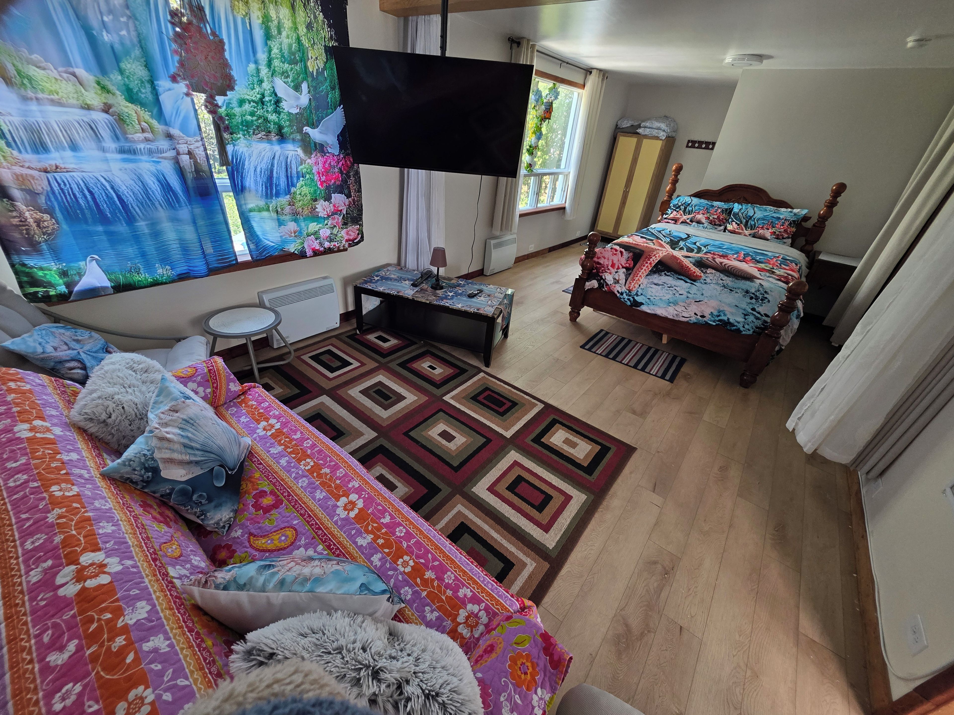A bedroom with a large bed, a smaller bed, a TV, a desk, and a window with curtains.