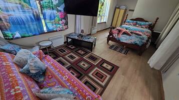A bedroom with a large bed, a smaller bed, a TV, a desk, and a window with curtains.
