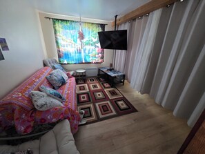 Un dormitorio con cama, televisor, una mesita y un ventanal con cortinas.