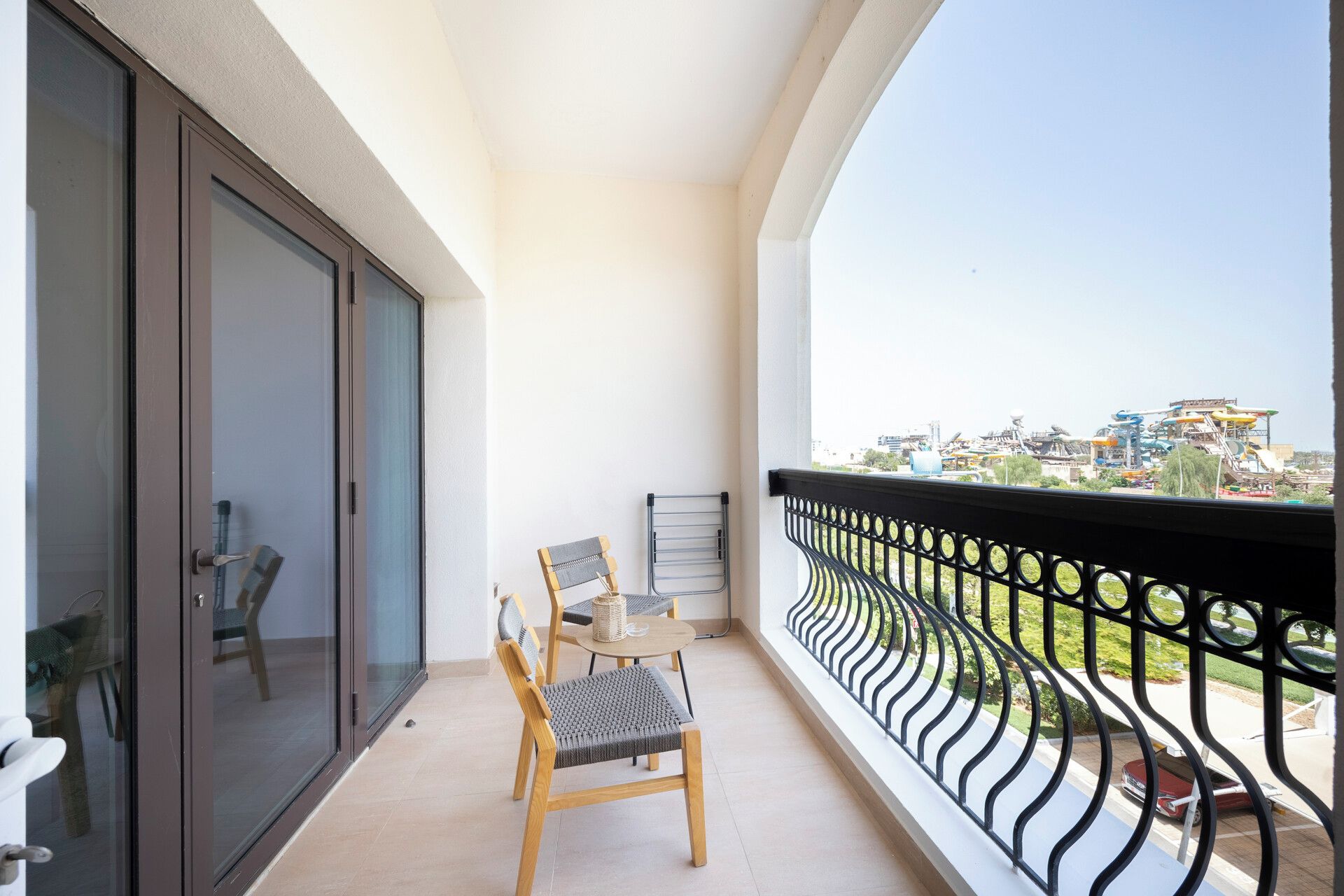 A balcony with a view of a cityscape, a sliding glass door, and a table with two chairs.
