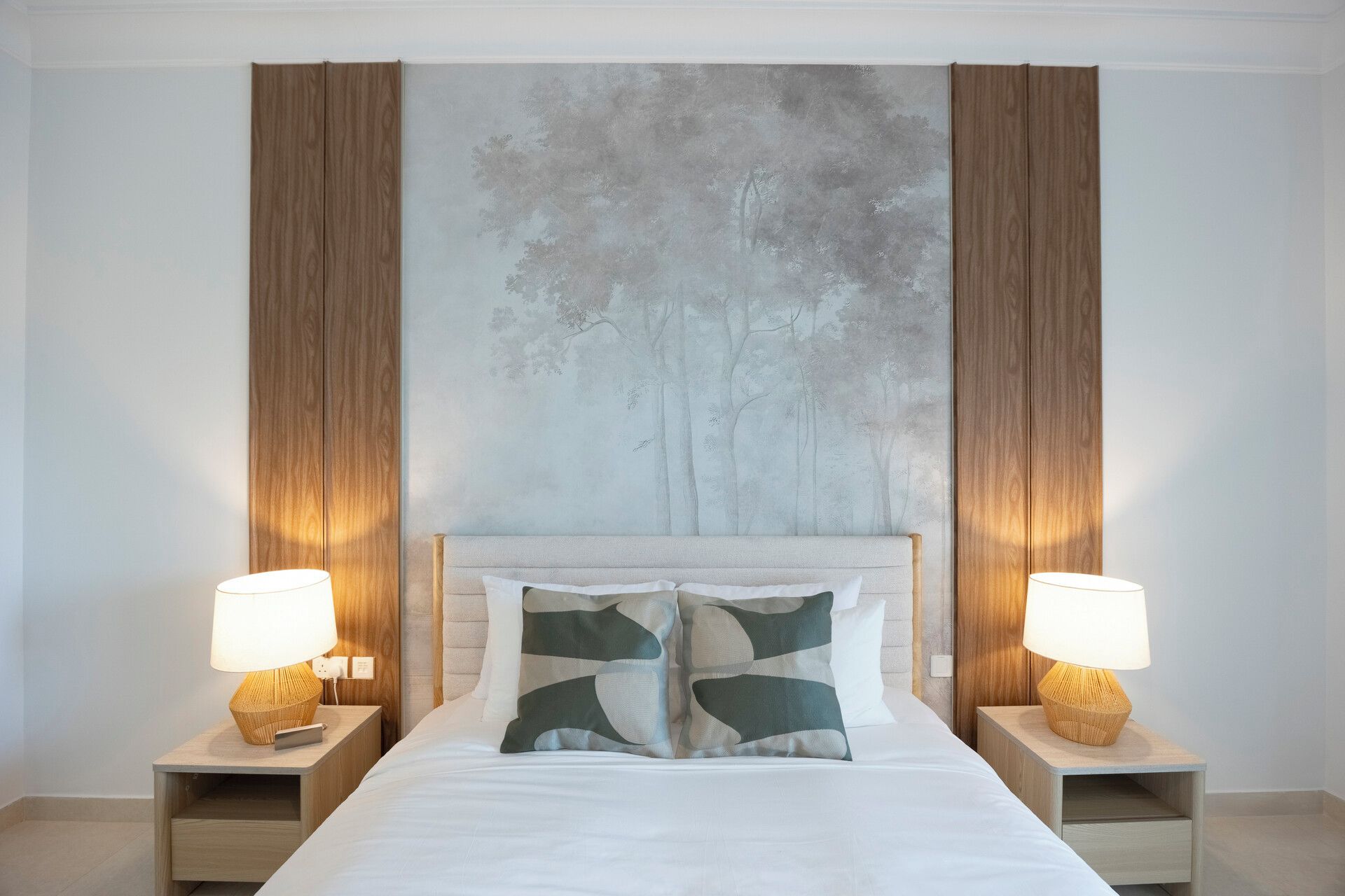 Ein Schlafzimmer mit einem Bett, zwei Nachttischen mit Lampen und einem großen abstrakten Wandbild.