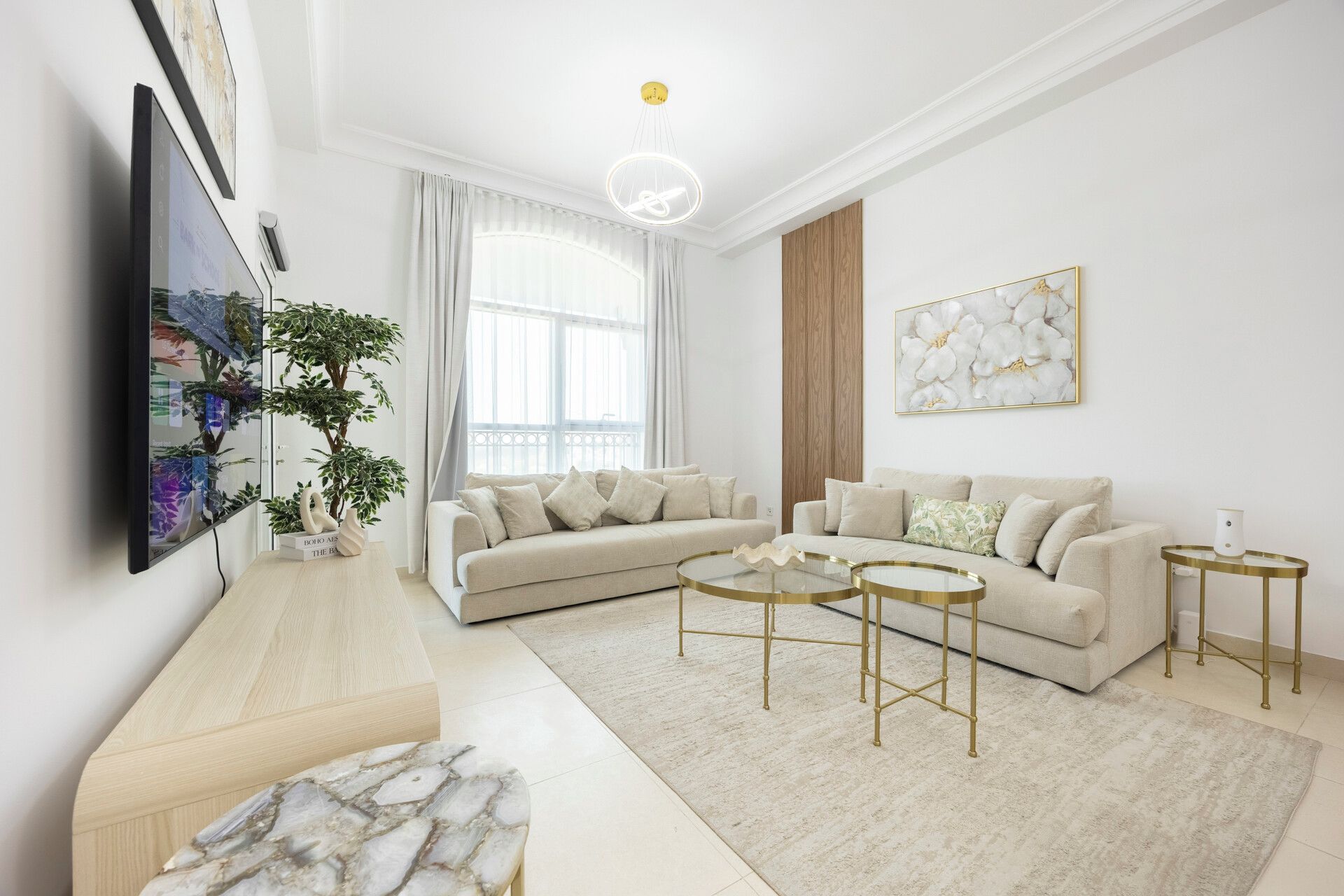 A modern living room with a sectional sofa, a glass coffee table, and a flat-screen TV mounted on the wall.