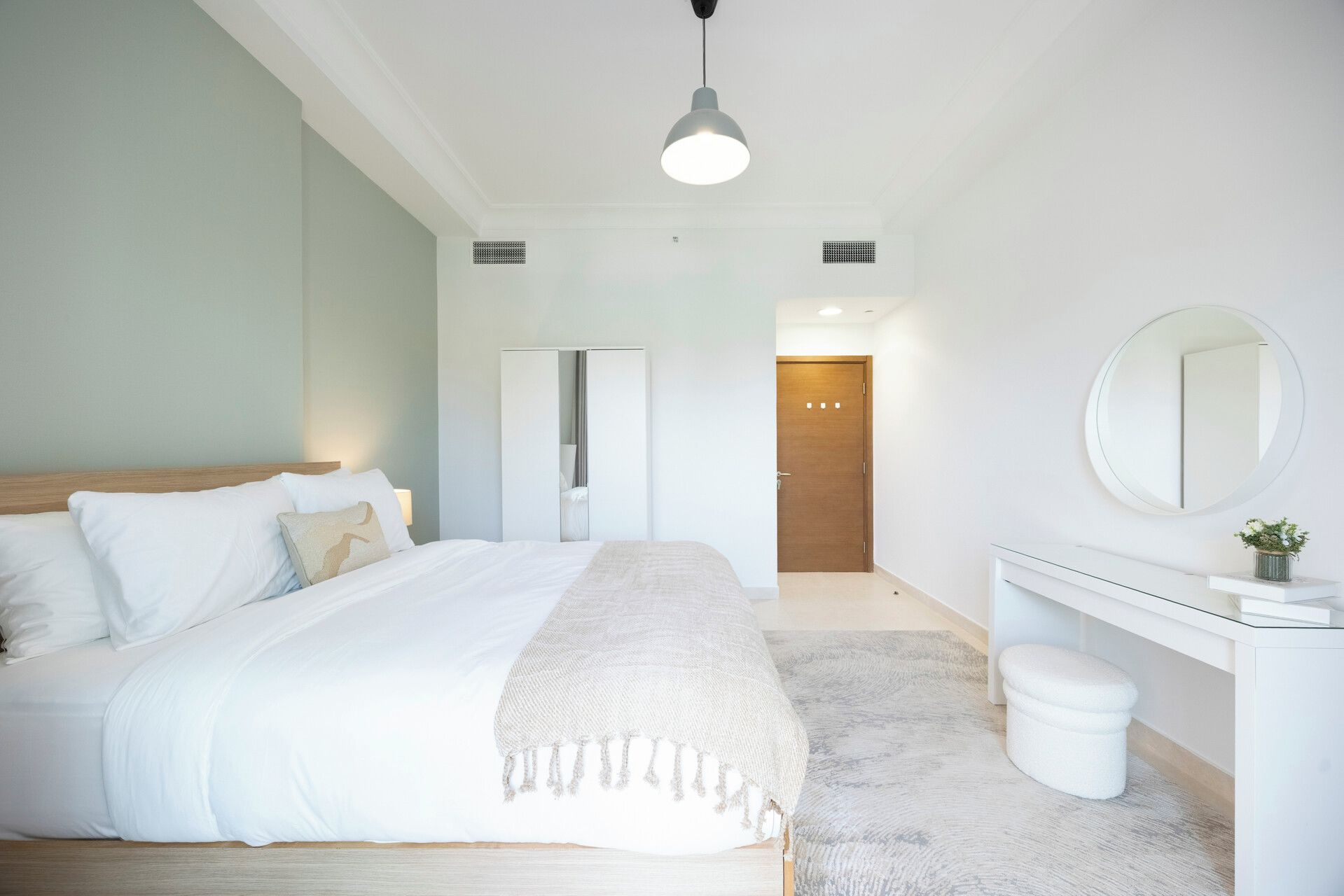 Een slaapkamer met een bed, nachtkastje, spiegel en een deur naar een andere kamer.