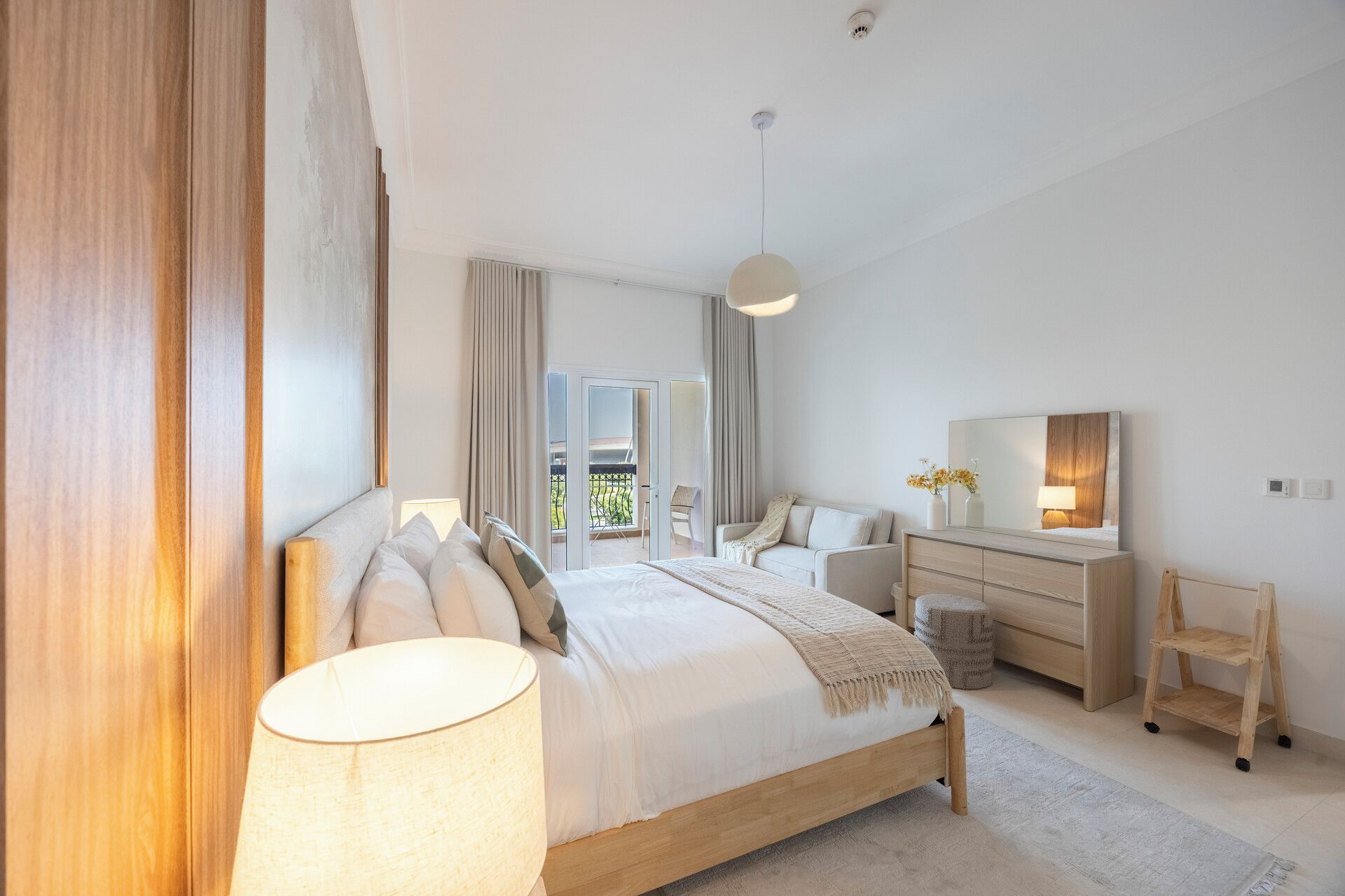Een moderne slaapkamer met een groot bed, nachtkastjes, een dressing en een spiegel.