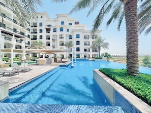Un hotel con piscina, palmeras y un edificio de varios pisos con balcones.