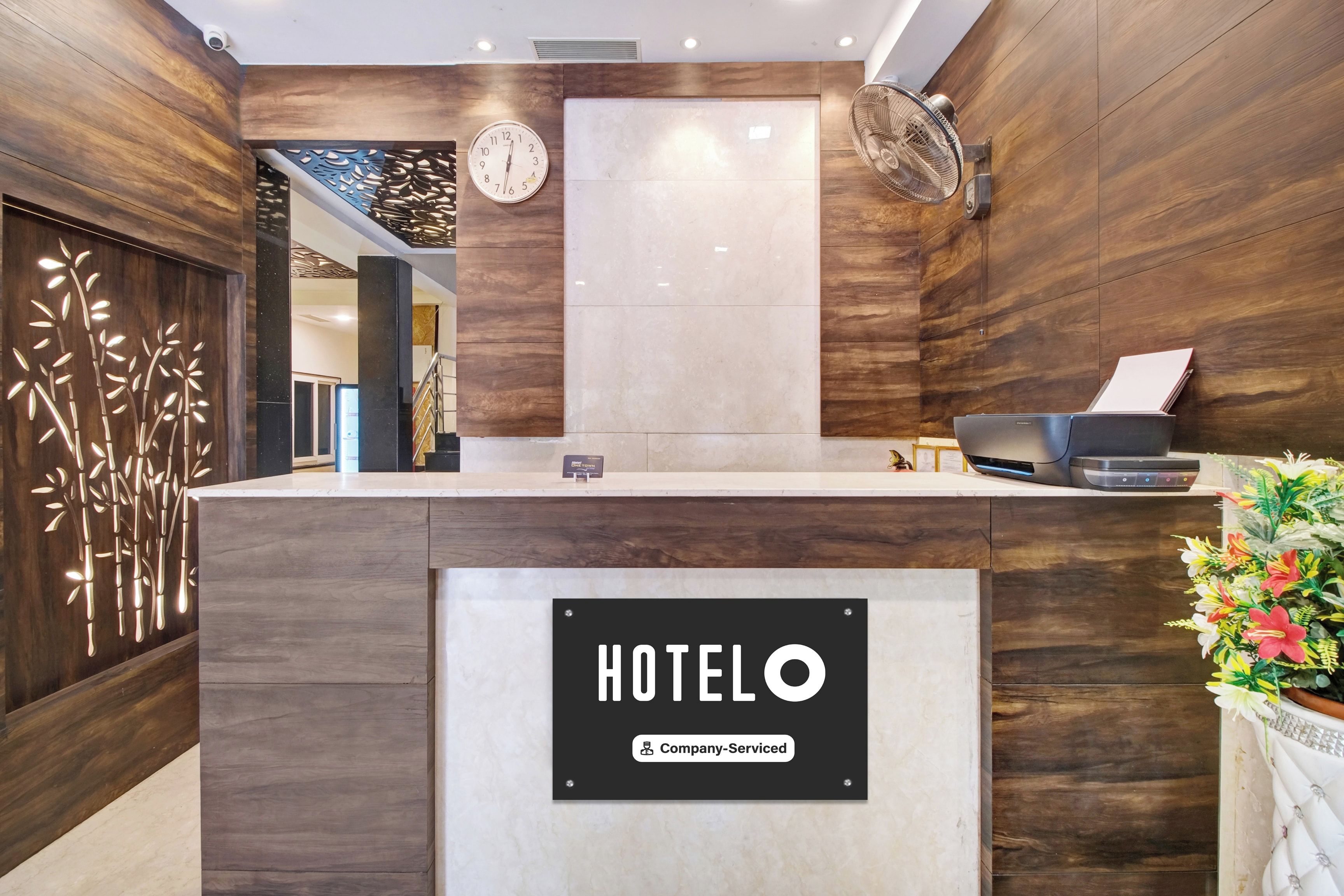 Una recepción de hotel con un reloj, un letrero de la empresa y un ventilador.