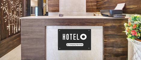 A hotel reception desk with a clock, a company-serviced sign, and a fan.