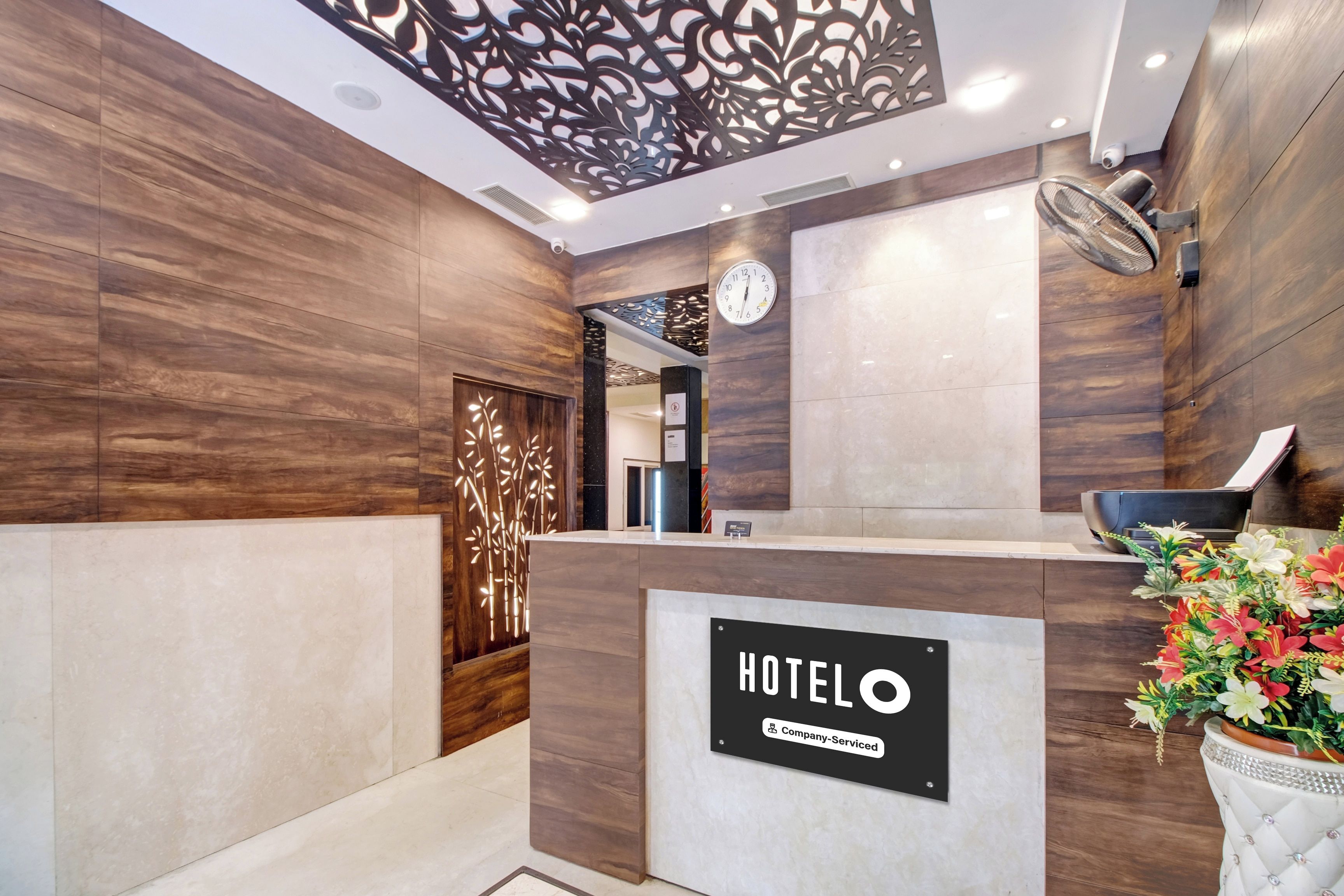 Zona de recepción de hotel con mostrador, un reloj y un panel decorativo en la pared.