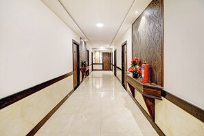 Un pasillo de hotel con piso de mármol, puertas de madera y un mostrador de recepción con extintor.