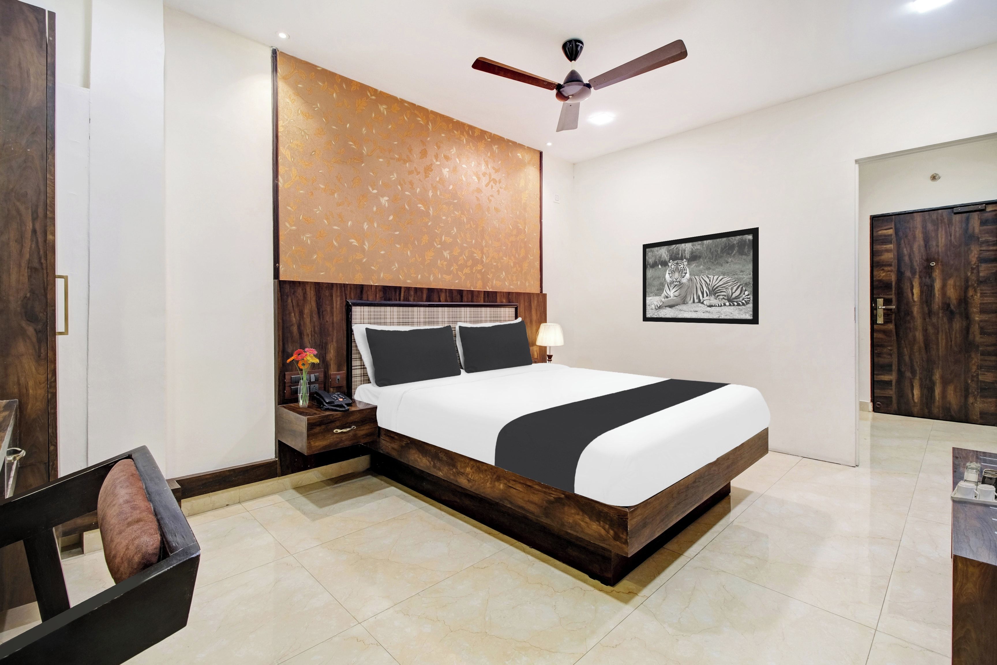 A hotel room with a large bed, a ceiling fan, a framed picture on the wall, and a wooden door.