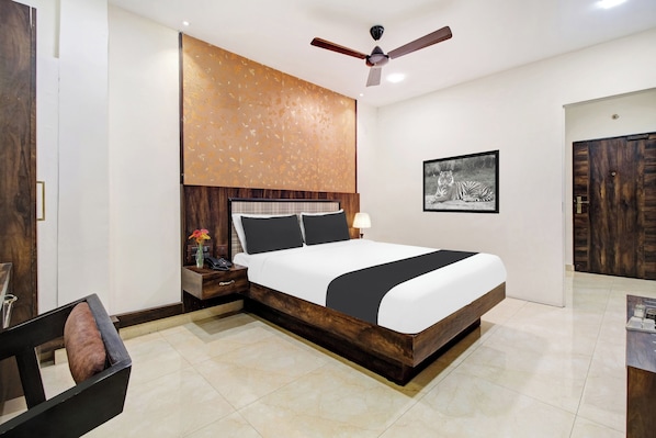 A hotel room with a large bed, a ceiling fan, a framed picture on the wall, and a wooden door.