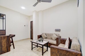 Uma sala de estar com sofá, mesa de centro, TV e ventilador de teto.