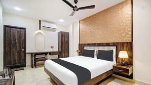 A hotel room with a large bed, a desk, a chair, a nightstand with a lamp, and a ceiling fan. - Hotel O Vijayawada Near Railway Station (Vijayawada)