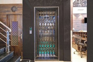 Um elevador moderno com porta em grade de metal, parede de madeira com ventilação e escada com corrimãos de metal.