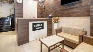 A hotel reception area with a reception desk, a sofa, a coffee table, a clock, and a TV mounted on the wall. - Hotel O Vijayawada Near Railway Station (Vijayawada)