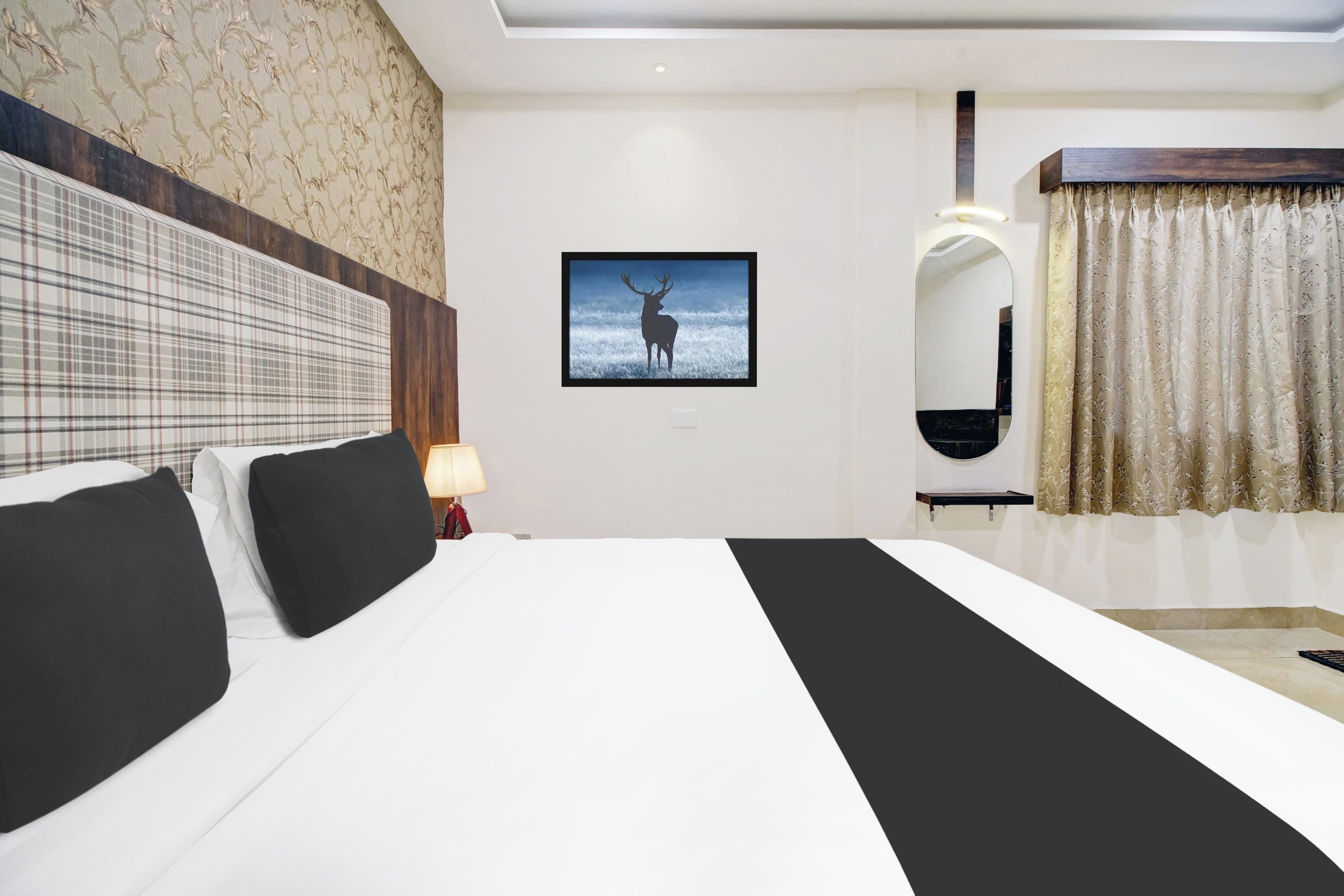 A hotel room with a large bed, a framed picture of a deer, a mirror, and a window with curtains.