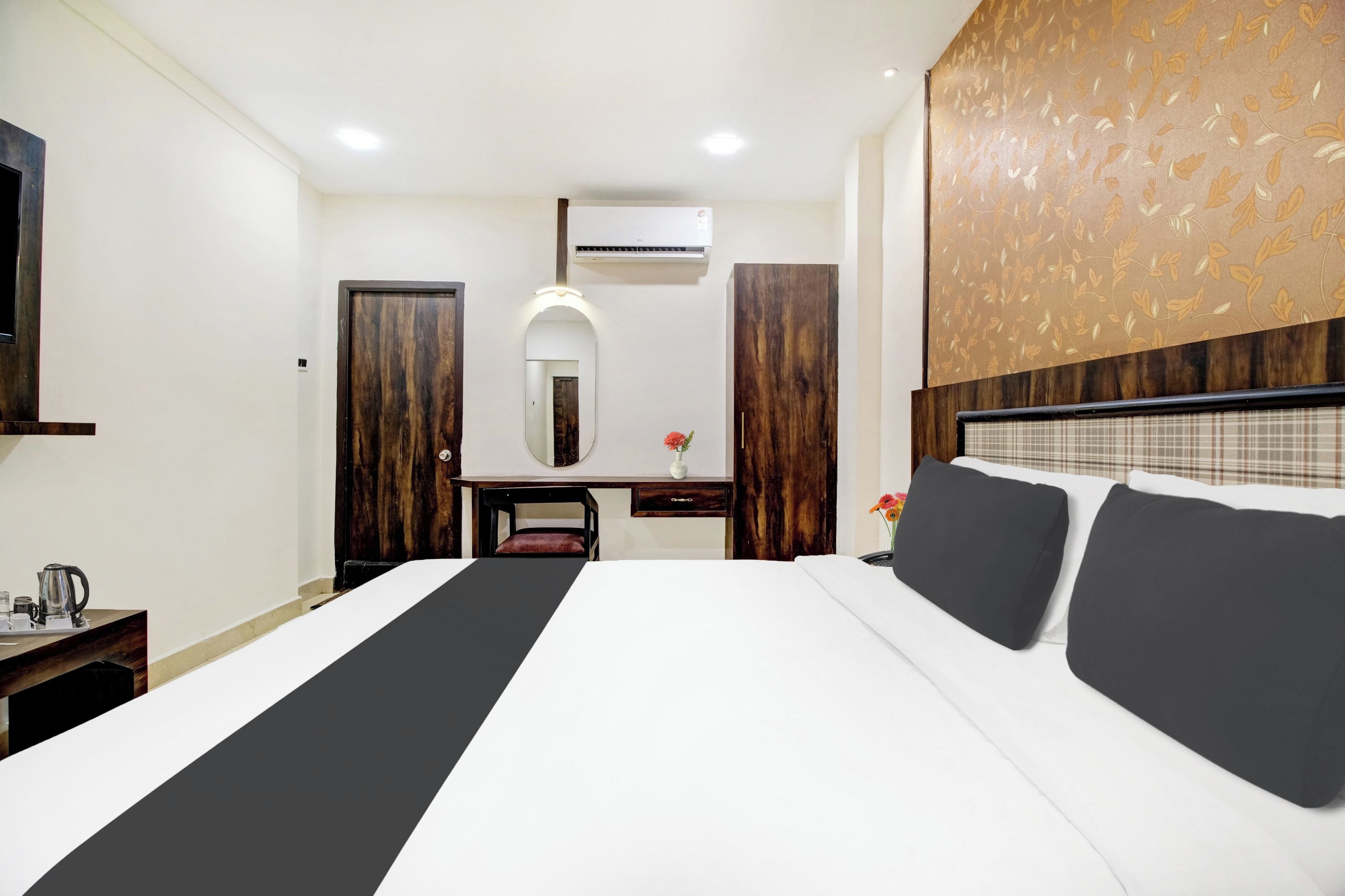 A hotel room with a large bed, a desk, a mirror, and an air conditioning unit.