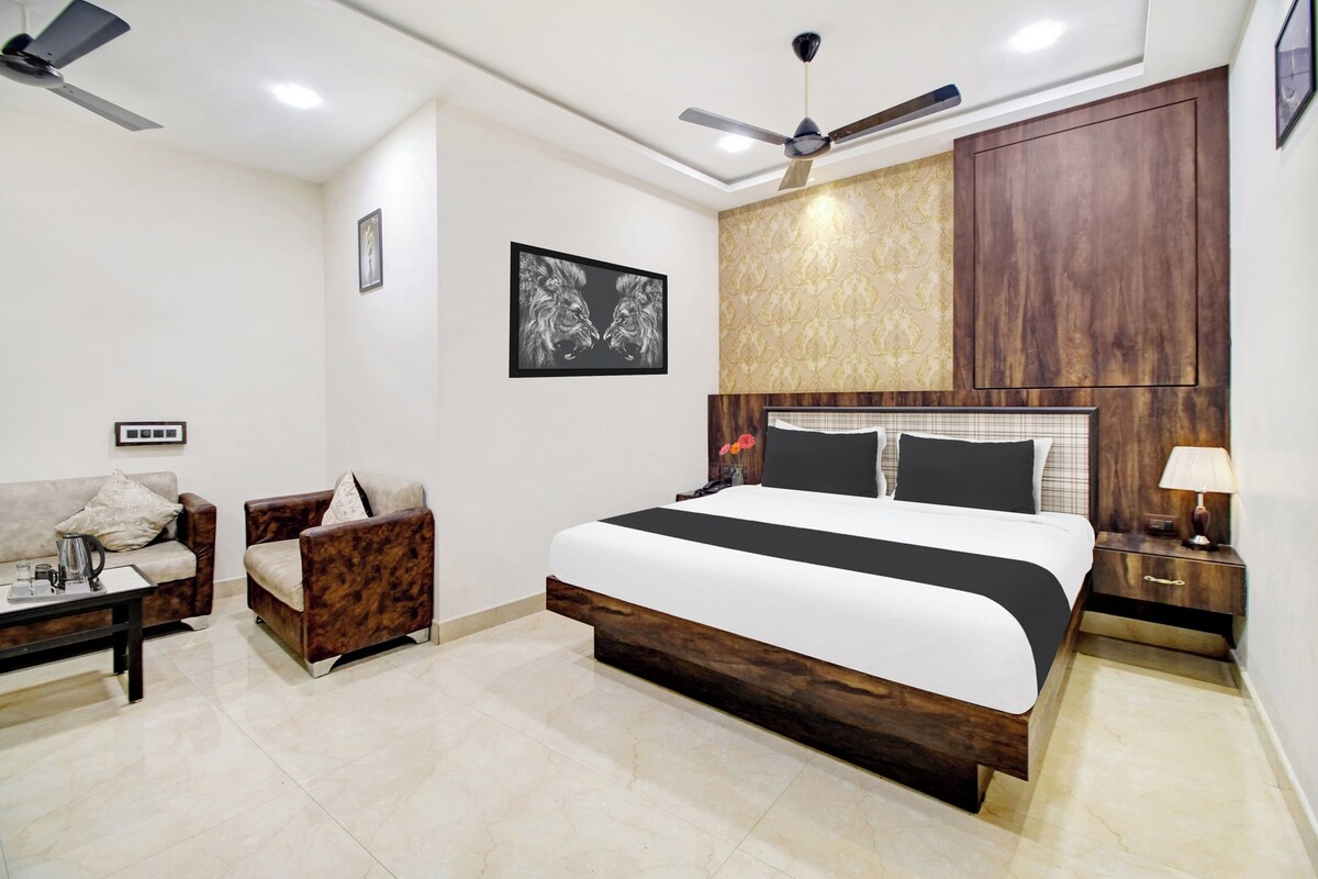 A modern bedroom with a large bed, a sofa, a chair, a nightstand, a lamp, and a ceiling fan.