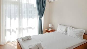 A hotel room with a bed, a nightstand, an air conditioning unit, and a view through the window.