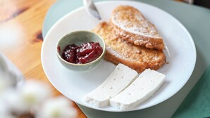 A plate with a slice of cake, a small bowl of jam, and two pieces of cheese on a table.