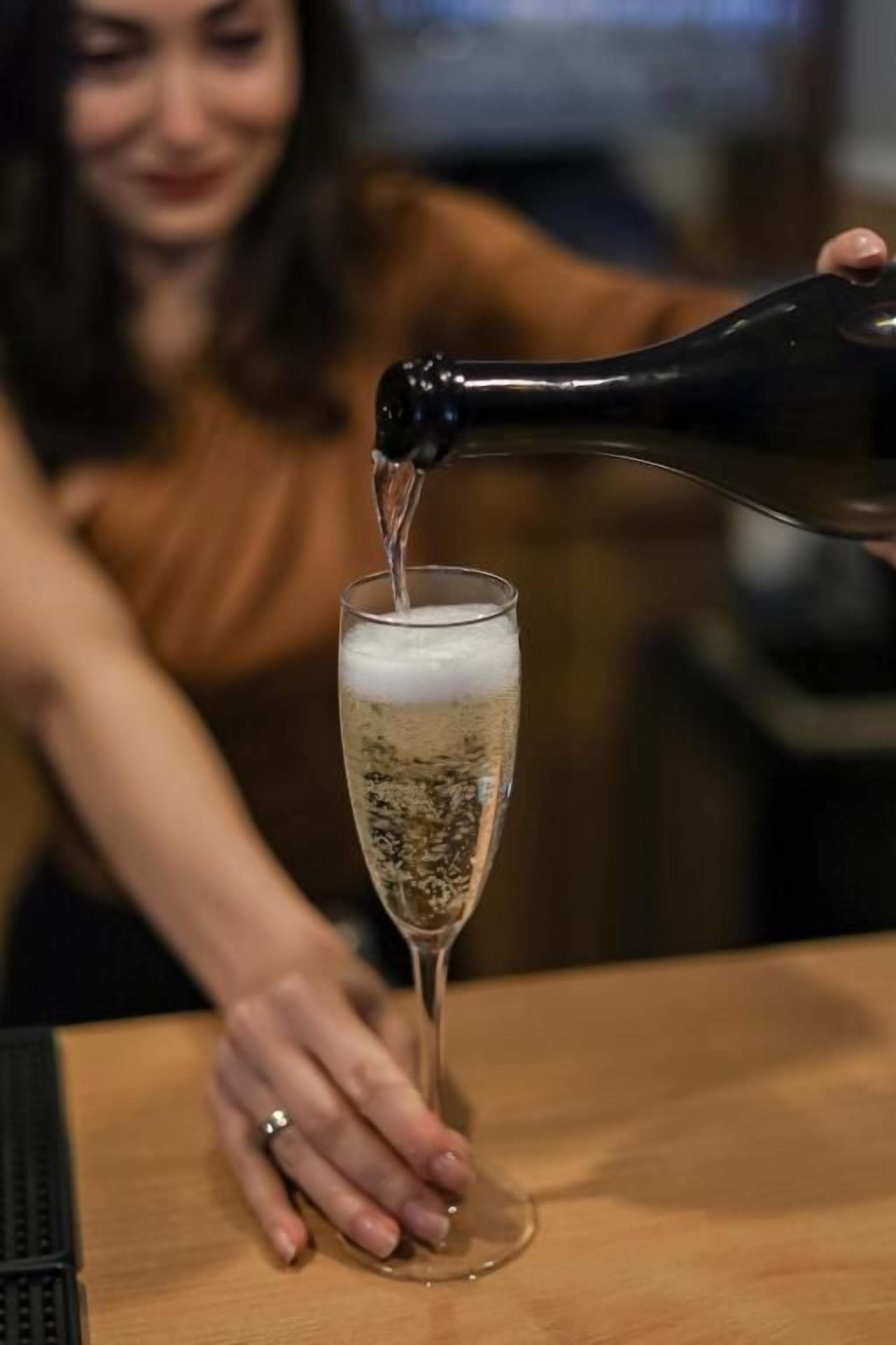 Una persona vertiendo un líquido de una botella a un vaso sobre una mesa de madera.
