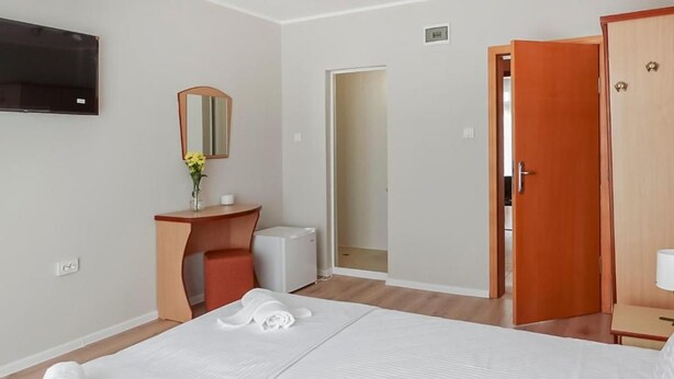 A hotel room with a bed, a desk, a mirror, a TV, and a door.