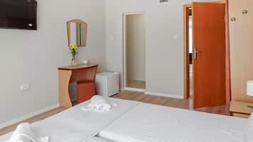 A hotel room with a bed, a desk, a mirror, a TV, and a door.