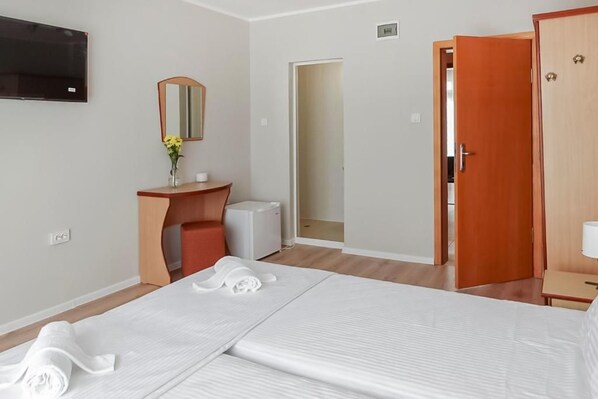 A hotel room with a bed, a desk, a mirror, a TV, and a door.