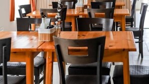 A restaurant with multiple tables and chairs, a wooden wall, and an air conditioning unit.