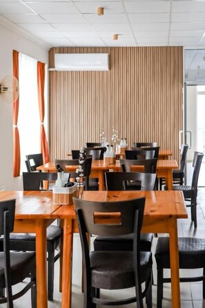 A restaurant with multiple tables and chairs, a wooden wall, and an air conditioning unit.