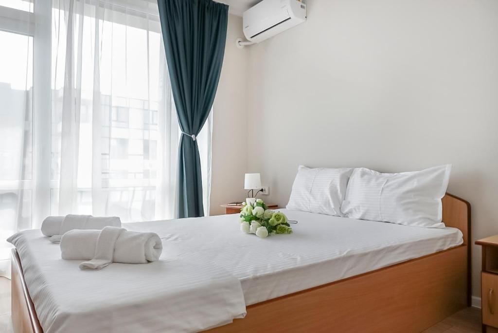 Ein Hotelzimmer mit einem Bett, einem Nachttisch, einer Lampe, einem Blumenstrauß und einer Klimaanlage.