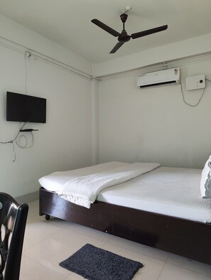 A bedroom with a bed, a ceiling fan, a TV, and an air conditioning unit. - Hotel Arika (North Lakhimpur)