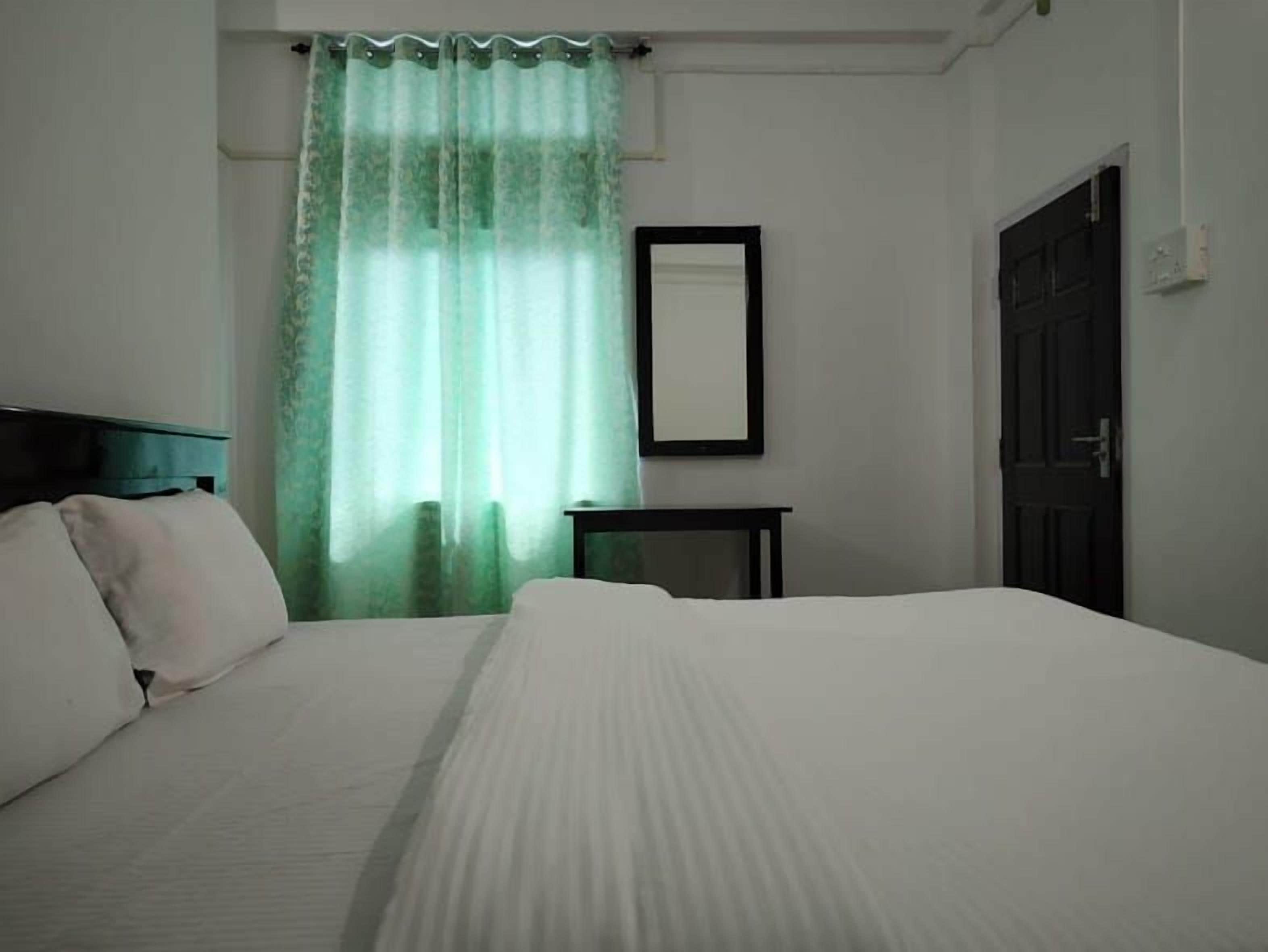 A bedroom with a bed, a nightstand, a mirror, and a door.