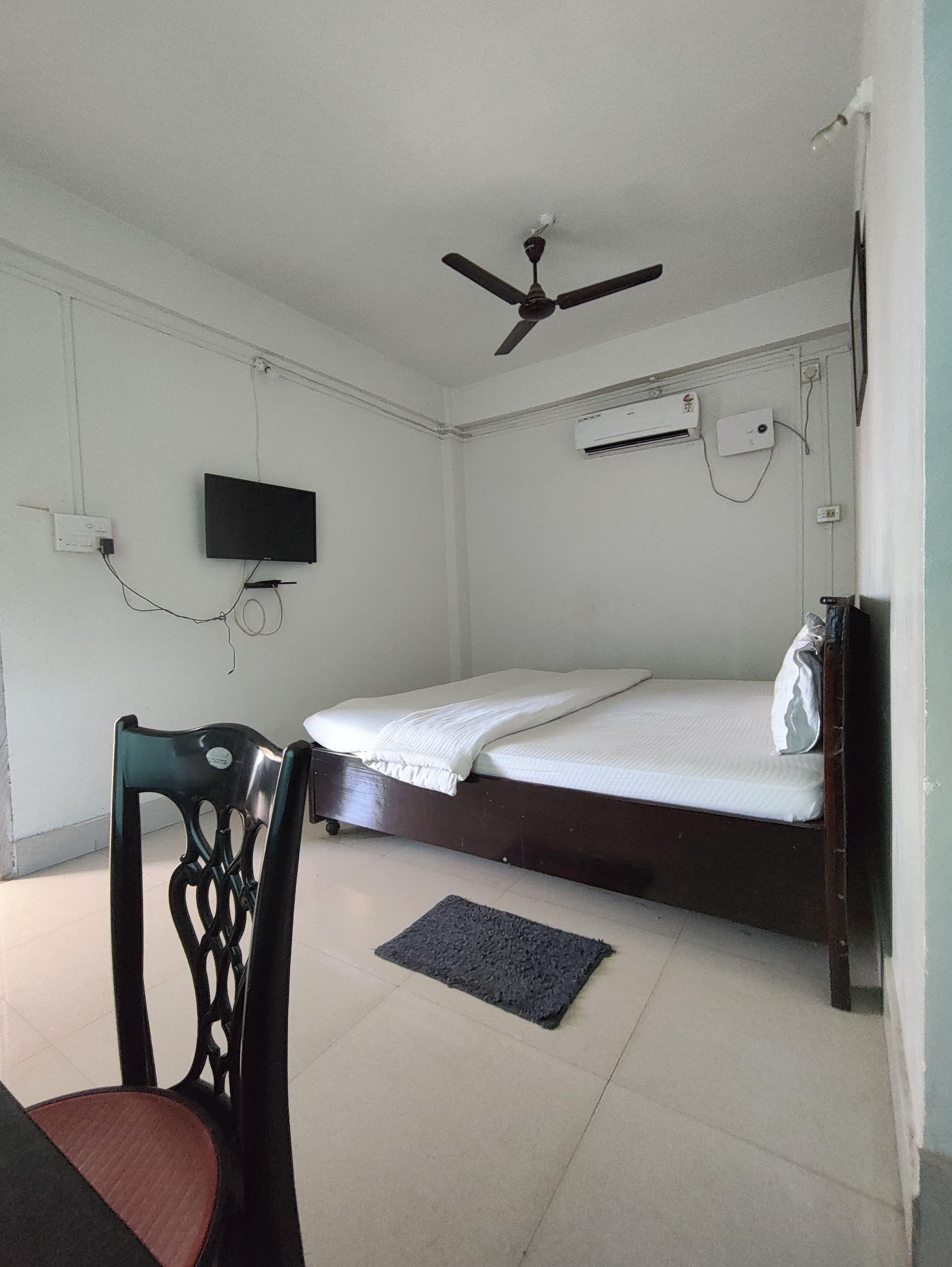 A room with a bed, a chair, a ceiling fan, a TV, and an air conditioning unit.