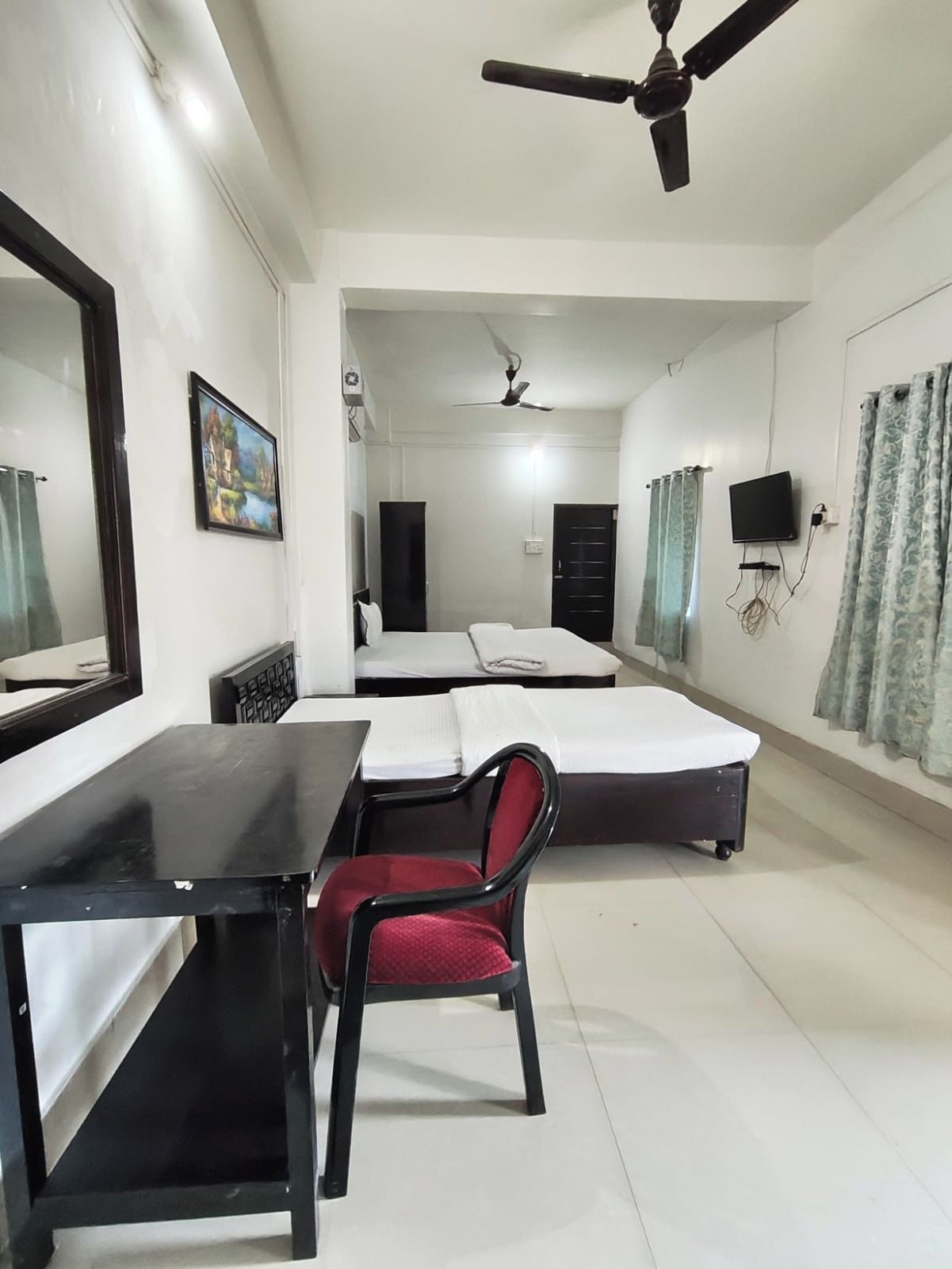 A hotel room with a bed, a desk, a chair, a television, and a ceiling fan.