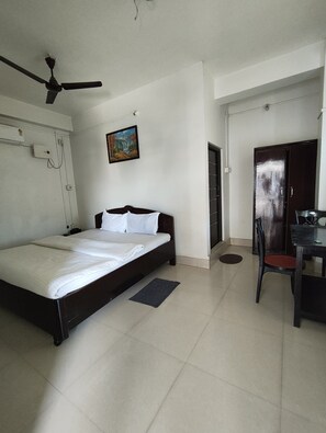 A bedroom with a bed, a desk, a chair, a ceiling fan, a painting, and a wardrobe.