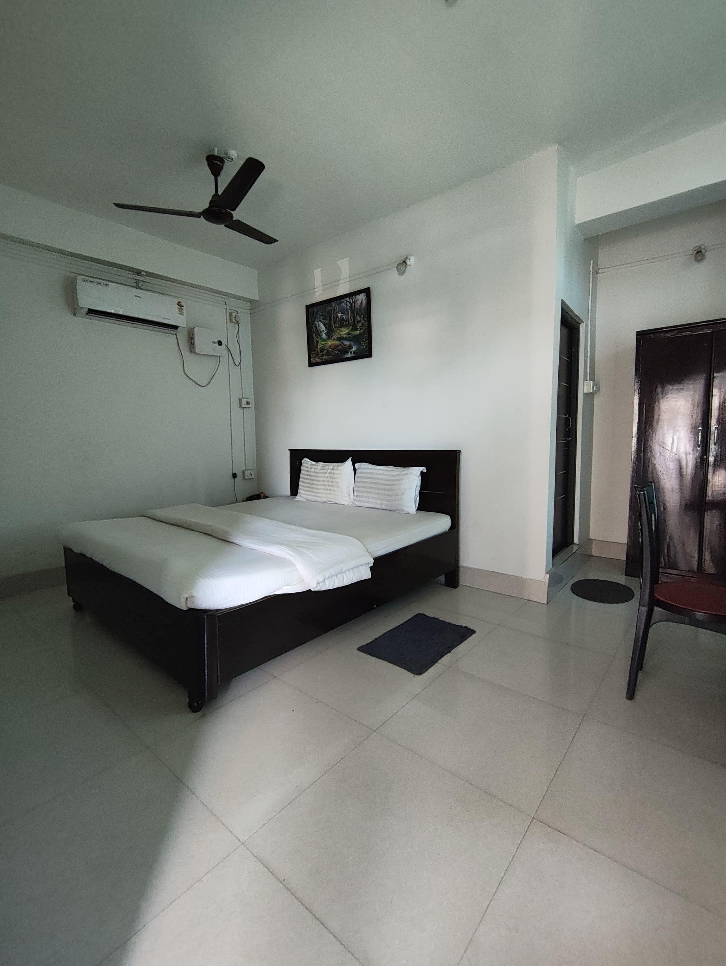 A bedroom with a bed, a ceiling fan, an air conditioning unit, a painting, and a door.