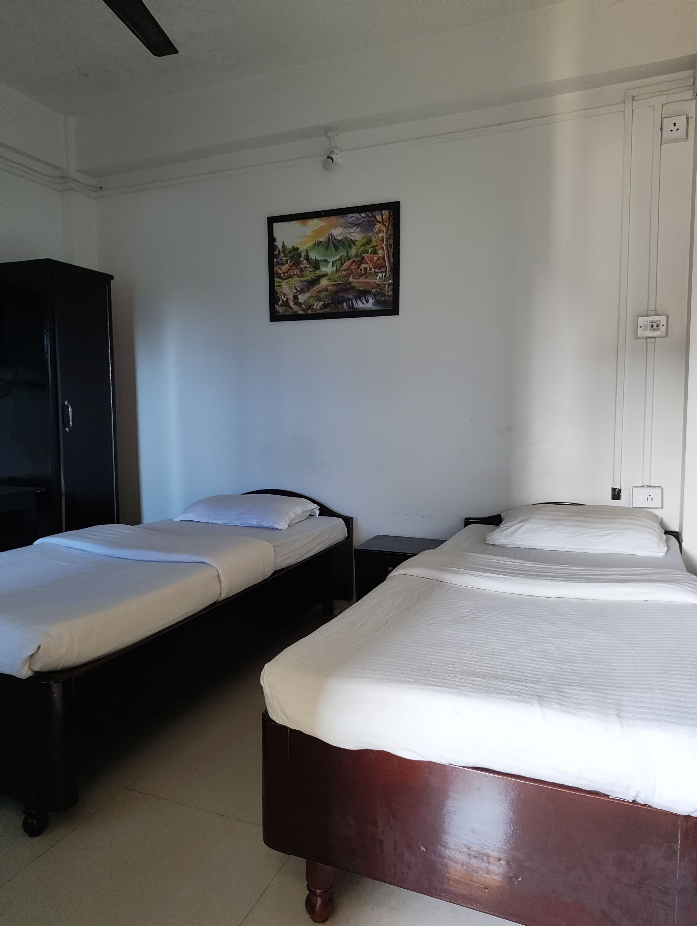 A room with two beds, a wardrobe, and a painting on the wall.
