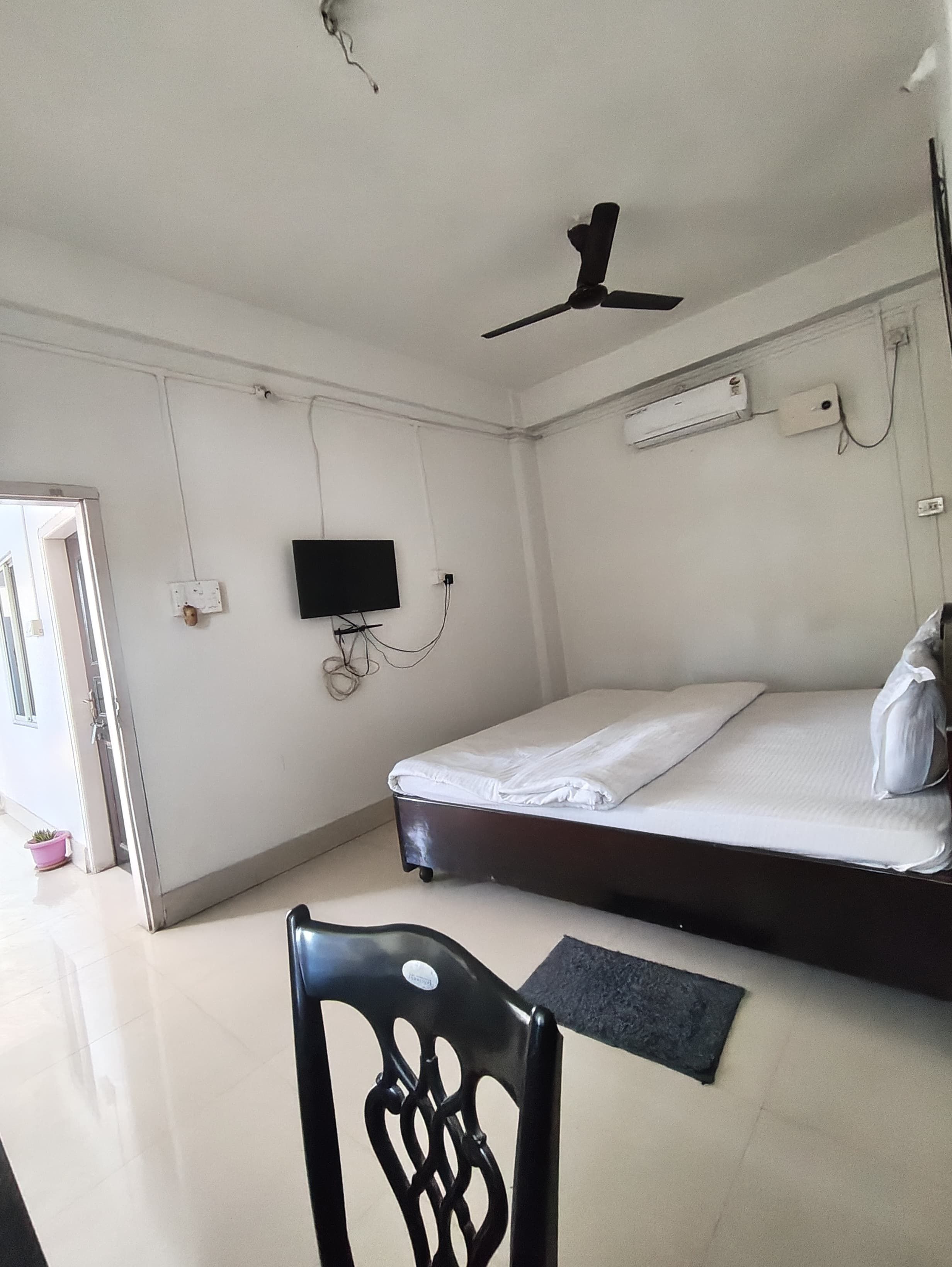 Un dormitorio con cama, ventilador de techo, televisor y puerta que da a otra habitación.