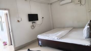 Un dormitorio con cama, ventilador de techo, televisor y puerta que da a otra habitación.